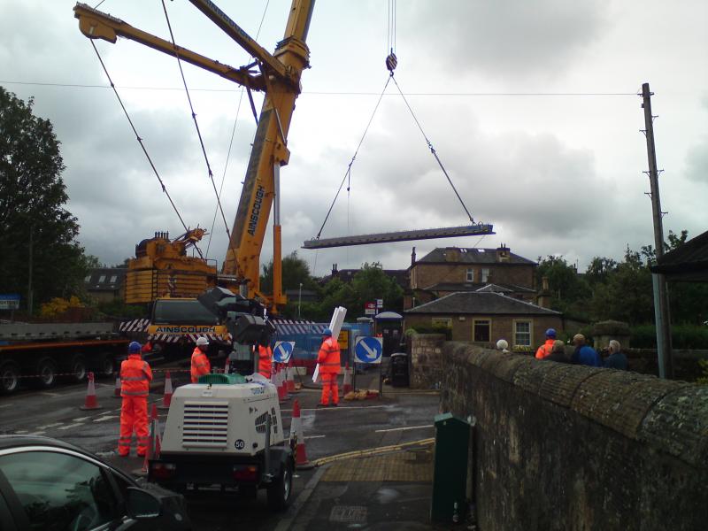 Polmont bridge replacement: The crane is lifting the first of the new concrete beams into place, slewing over the station building, on 14 June 2015 Photo of Polmont bridge replacement