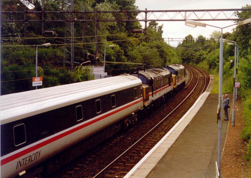 Monarch of the Glen: Not the TV series but the InterCity Land Cruise which used to run between London and Fort William and Mallaig.
Headed by 37221 and 37152 a return MOG in the rural surroundings of Drumchapel in July 1993. Photo of Monarch of the Glen